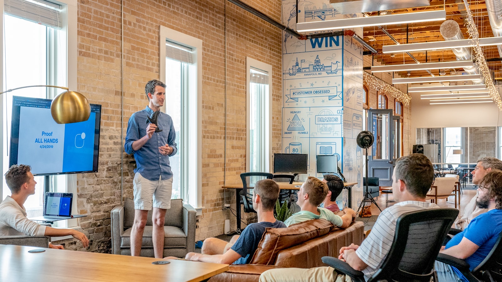 A team gathered on sofas for an all-hands presentation in a converted brick office