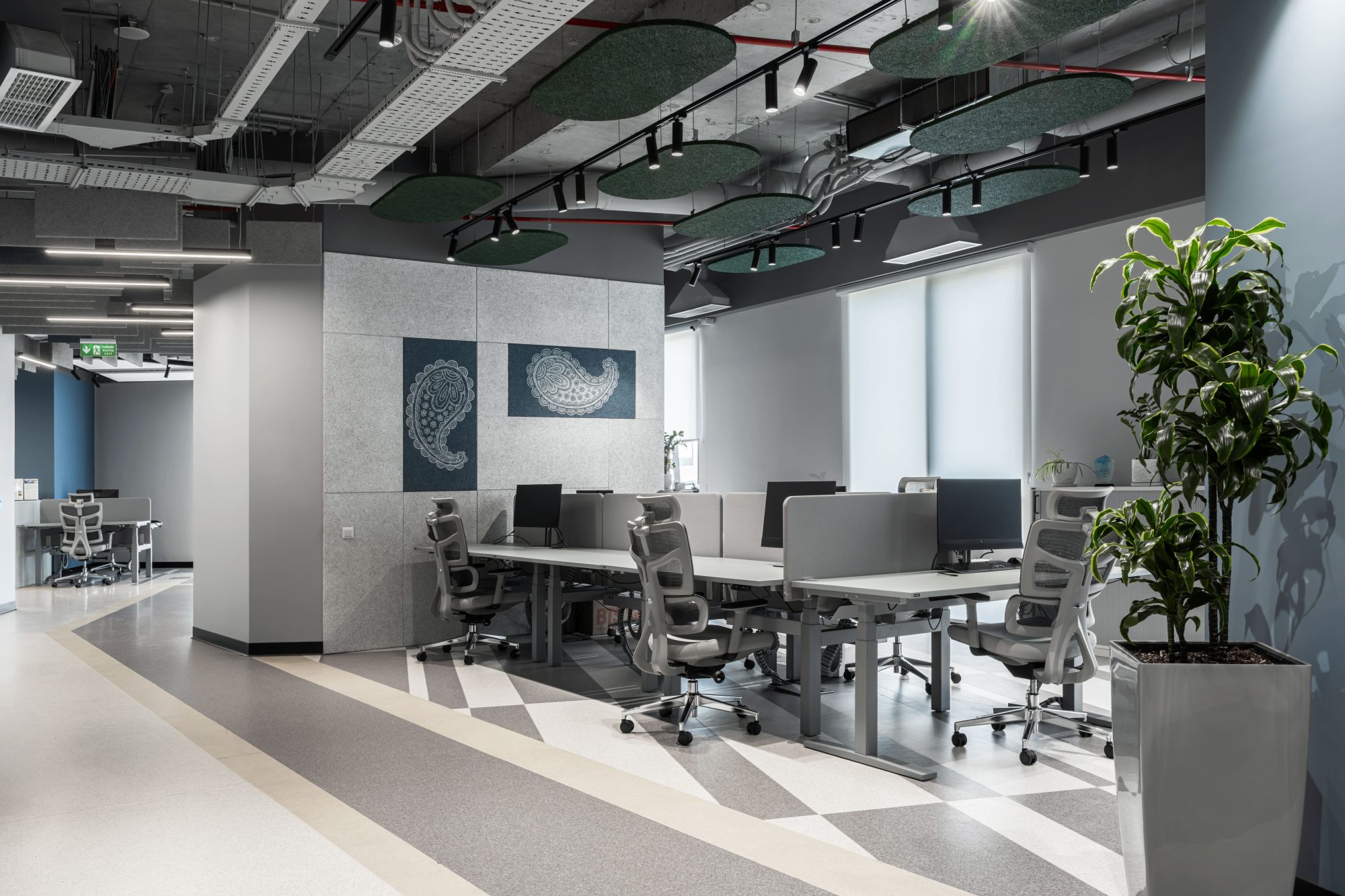An empty break out area with a bench, low shelving and a kitchenette beside a glass walled corridor.