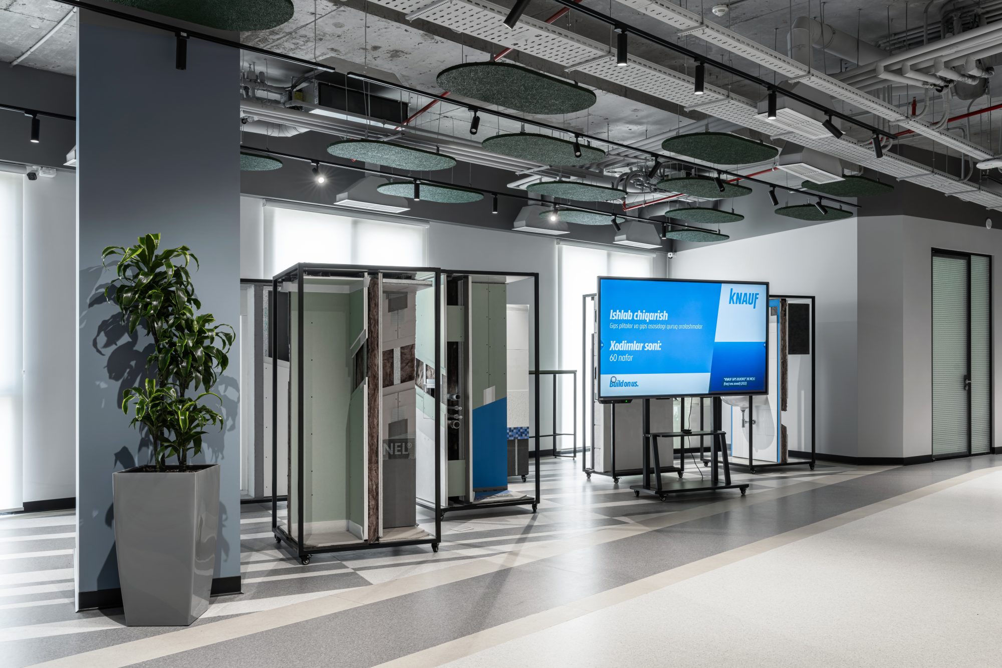A glass walled corridor with a lounge area visible through the partitions, furnished with a sofa and a floor lamp.