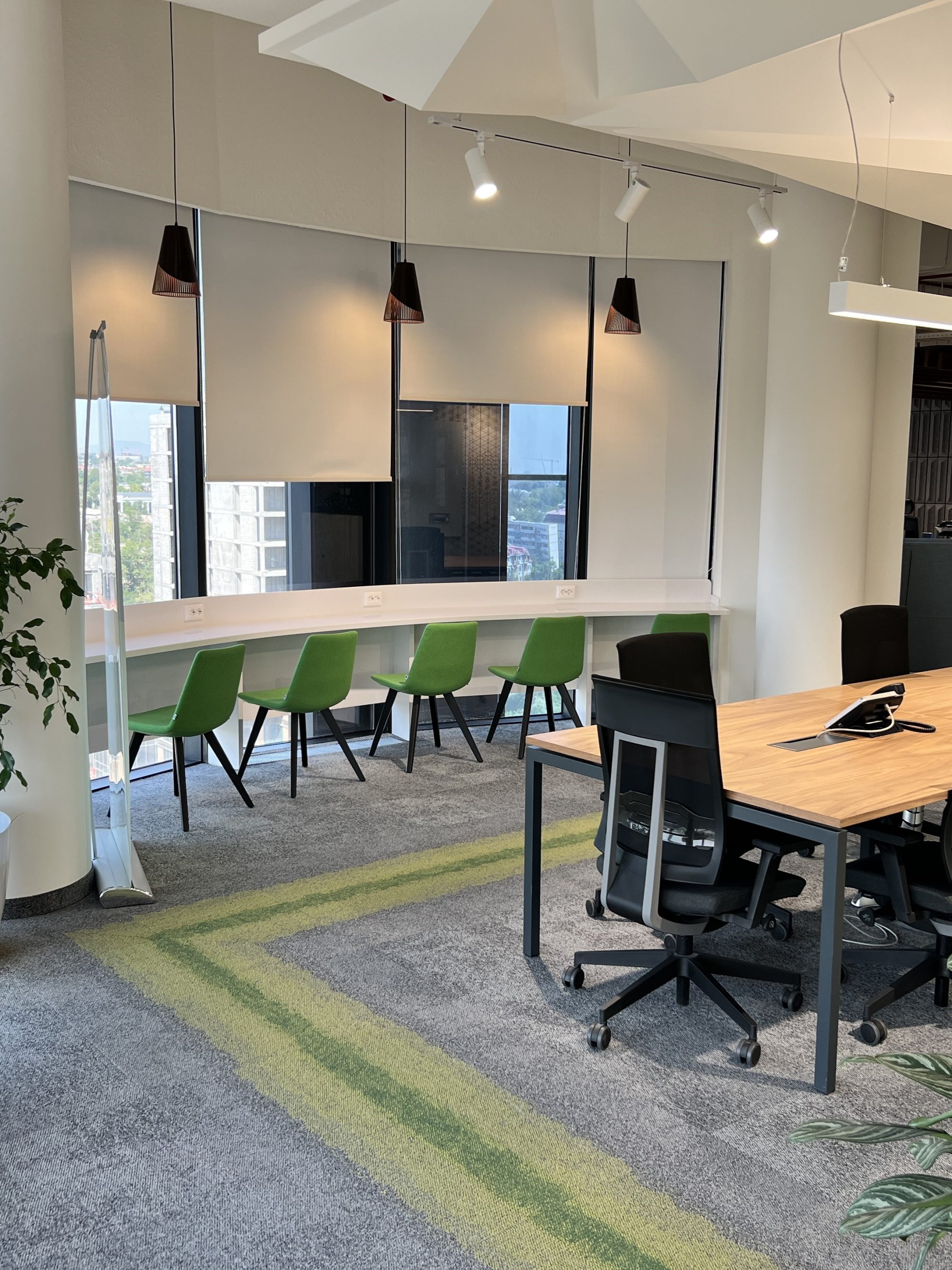 A plant filled lounge with green velvet armchairs, where three people talk at a table by the window.
