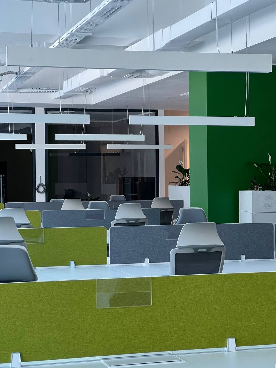 A glass walled corridor with a lounge area visible through the partitions, furnished with a sofa and a floor lamp.