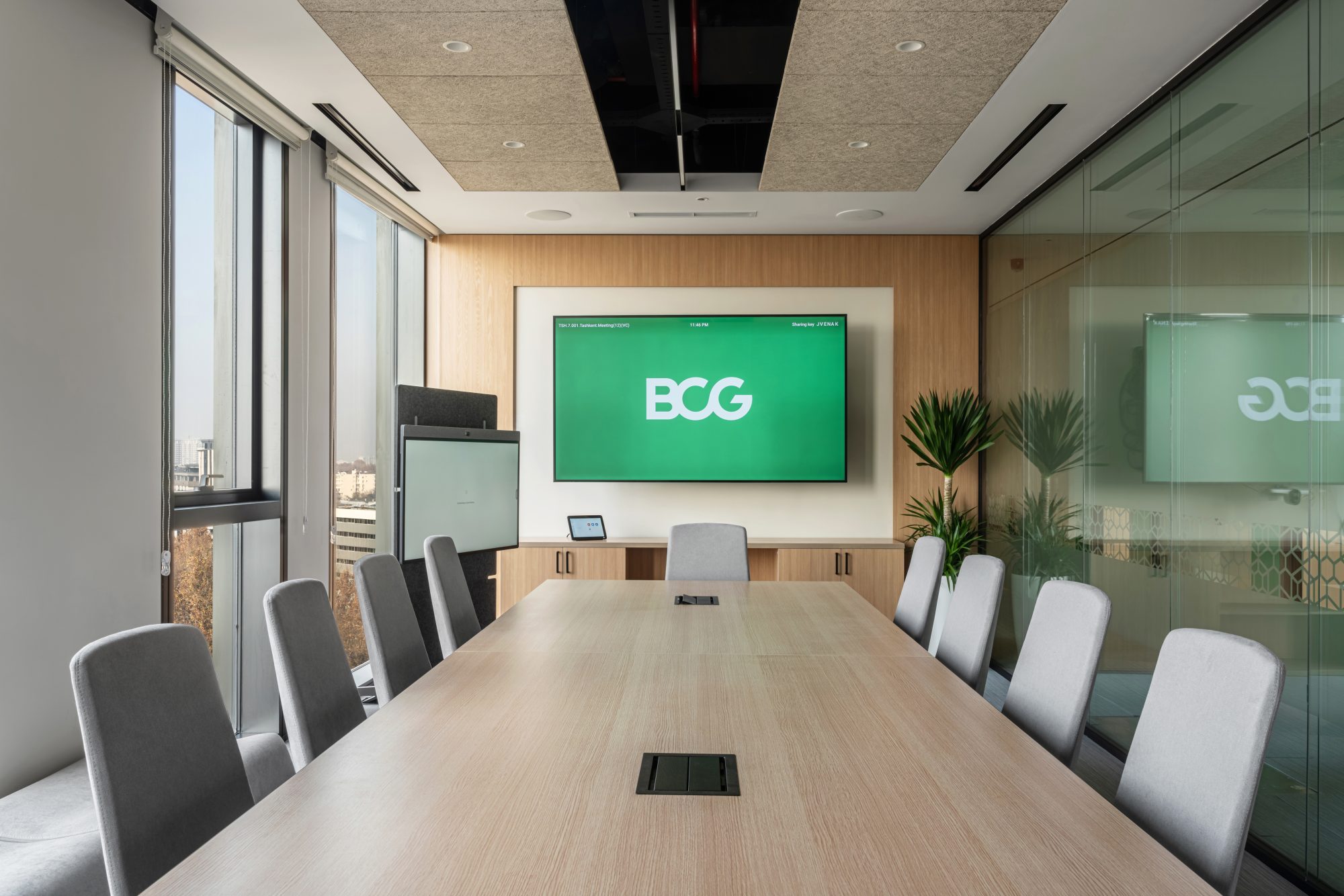 A meeting room with a rough wooden table, white chairs and a floor to ceiling window overlooking the city.