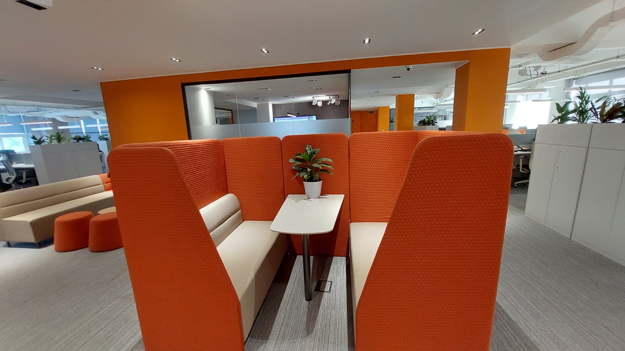 A plant filled lounge with green velvet armchairs, where three people talk at a table by the window.